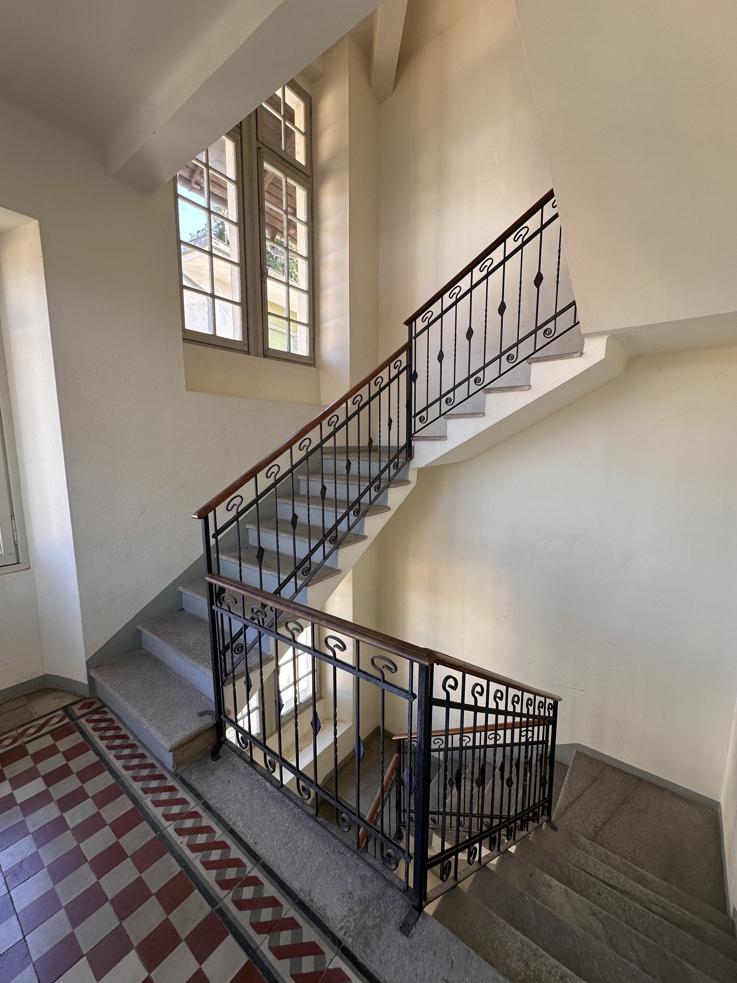 Cage d'escalier avec rampe en fer forgé et carrelage rouge et blanc